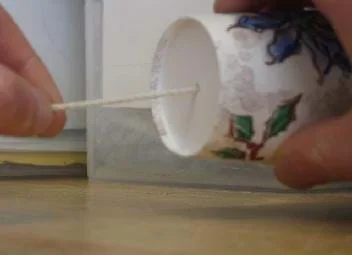 Photo shows one hand holding a paper cup sideways with a string coming out of the bottom and fingers of another hand pulling the string tail taut and away from the cup.