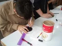 A student cuts a hole in the lid of the oatmeal container using an Exact-o knife.