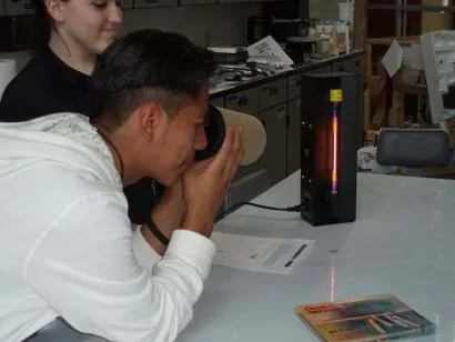 A student looks through a finished spectrograph at a gas discharge tube.
