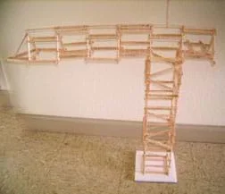 About 100 Popsicle sticks glued end-to-end to create a truss-like tower with a horizontal top structure longer on one side than the other.