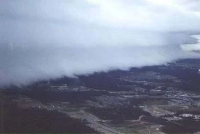 A photo shows bank of very thick, layered white clouds above a town.