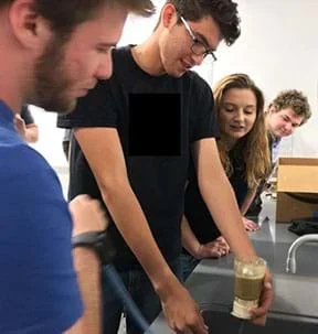 Four students set up a quicksand experiment over a lab sink using the vacuum filter with three students observing.