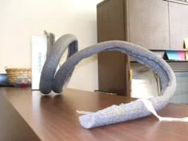Photo shows a coil of gray foam insulation taped to a desktop and textbook at opposite ends.