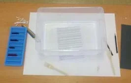 A photograph shows a tabletop with an ice cube tray containing 4 colors of ink, a 9 x 12-inch plastic frosted container, a few paintbrushes, Q-Tips, plastic forks, paperclips, pencil and paper.