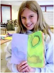 A photograph shows a girl holding a colorful packet of paper covered with water-color looking free-form ink images.