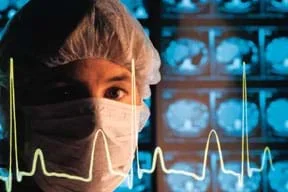 Photo shows a medical practitioner in a mask and surgical cap standing in front of a wall of illuminated x-rays. The familiar line blips of an electrocardiogram (heartbeat) are superimposed over the image.