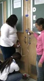 Three students standing by a door, measuring g.