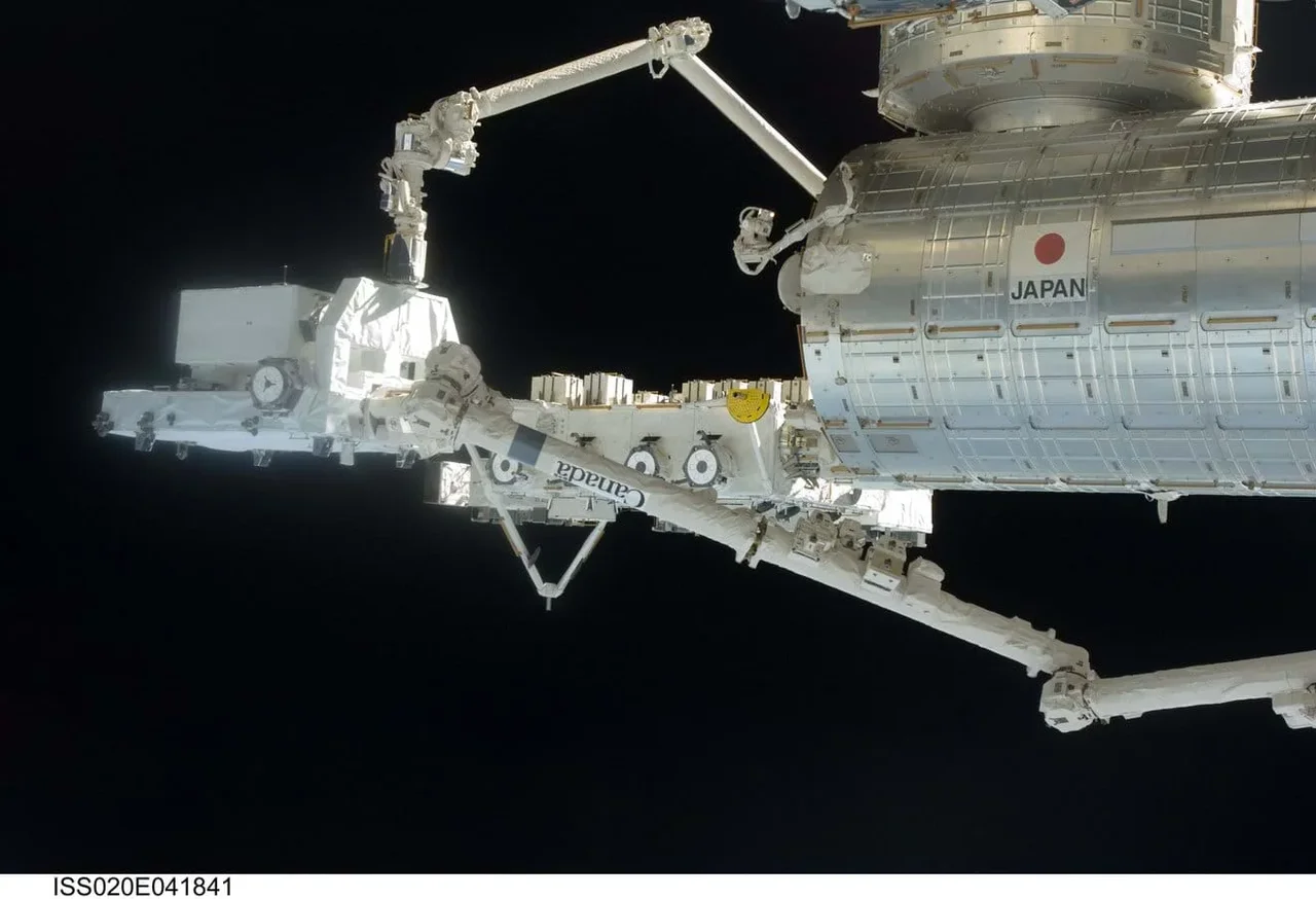 A photo showing a view of the International Space Station modules against the blackness of space. In the foreground, the Japanese Experiment Module (JEM), Kibo, is visible, labeled with the word 'JAPAN'. Attached to the module are two highly articulated robotic arms. The larger arm, which appears to be the JEM Remote Manipulator System (JEMRMS), extends horizontally, and a smaller, more delicate arm is positioned above it, showing the complex capabilities required for station assembly and maintenance.