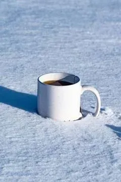 A photo showing a mug of dark liquid sitting on top of snow.