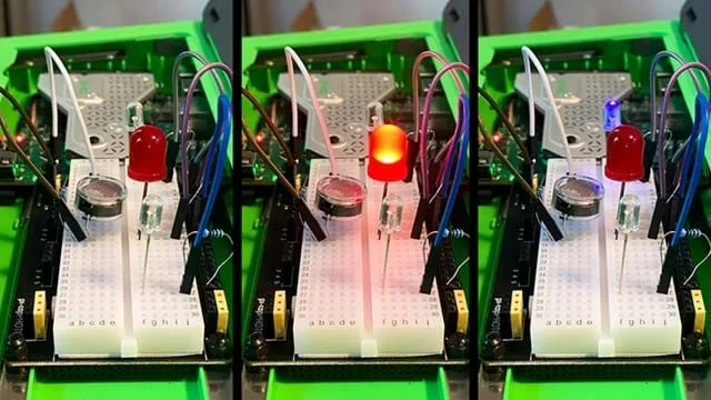 A photo showing a small electronics breadboard setup inside a green plastic case. The breadboard has several components inserted: three LEDs, a small circular sensor, resistors, and multiple jumper wires connecting the components to the underlying circuit board.