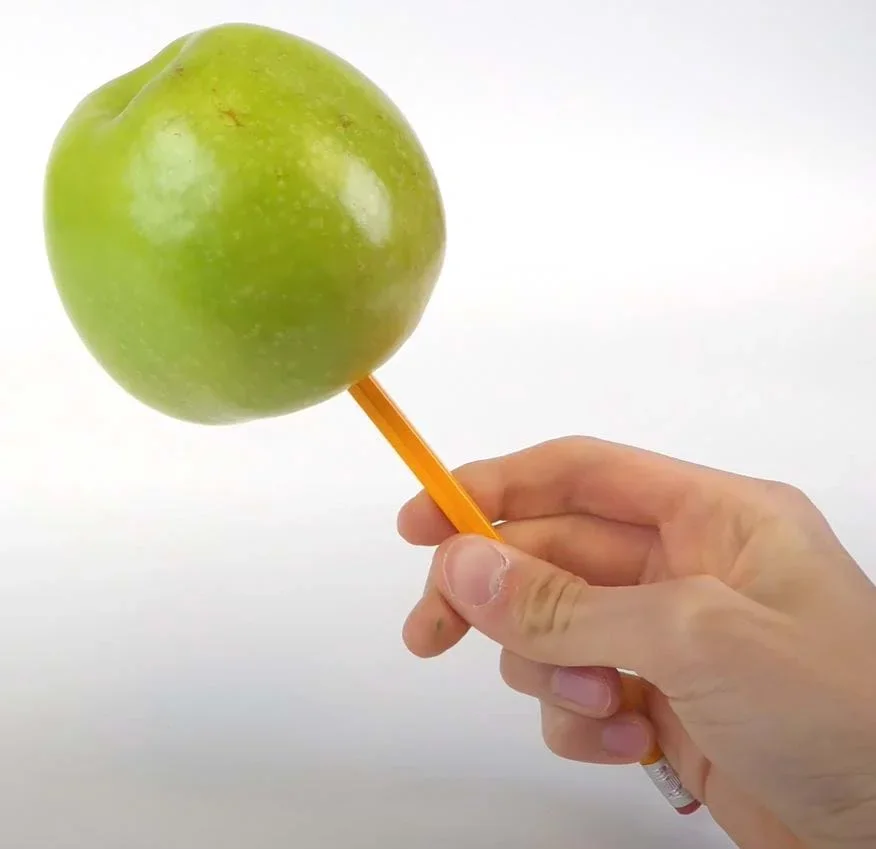 A green apple on the end of a pencil.