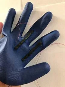 A blue rubber glove that has two black strips on the first two fingers. The black strips have a wire coming from each end of them.