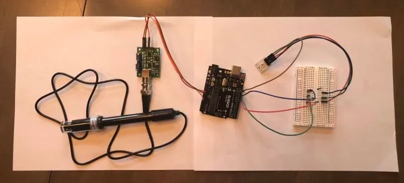 Photograph of an Arduino connected with wires and a breadboard to a pH sensor and LED module light.