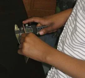 A photograph shows a student’s hands as he uses digital calipers to measure the depth of his assigned alloy.