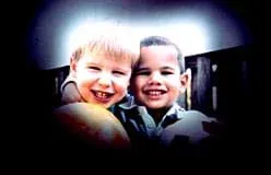 A photograph shows two smiling boys standing side-by-side, each holding a ball. The edges of the image are black, permitting only the center of the scene to be seen.