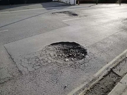 A photograph shows a generally smooth asphalt road with two potholes. One is circular and large. The other is smaller and more of an asphalt indentation.