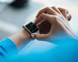 A photograph shows the right hands of a person pushing buttons a smart watch on her left wrist.