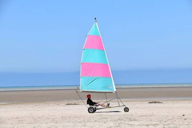 A man riding on a pink and blue vehicle that transforms the (kinetic) energy in wind to usable energy for vehicular motion.
