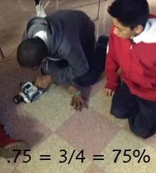 A photo shows two young boys sitting on a classroom floor as they work with a LEGO EV3 robot.