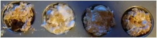 A photograph from above shows a row of a metal muffin tin in which the four cups are filled with a mixture of Rice Krispies® cereal and melted marshmallows.