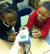 Two children at a table with a hand-held robot.