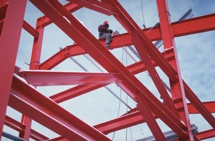 Photo shows a network of red steel beams under construction.