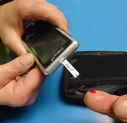 Photo shows a person testing his/her glucose level using an electronic device after taking a tiny sample of blood from a finger.