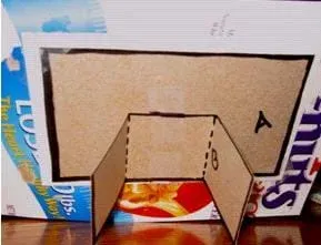 Photo shows the long folded cardboard rectangle piece supporting the larger picture frame cardboard piece.