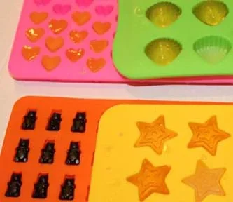 An image of hydrogels prepared in molds of different sizes, shapes, and colors. The hydrogels are yellow, orange, and blue while the molds are made up of pink hearts, lime green shells, orange gummi bears, and yellow stars.