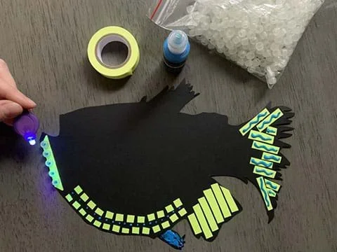 An aquatic organism cut-out on black cardstock expressing bioluminescence with fluorescent materials such as glow-in-the-dark tape, UV beads, and glow paint.