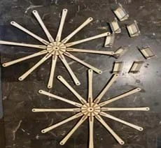 A disassembled small wooden model Ferris wheel sits on a table. There are two circular pieces with arms and seven baskets.