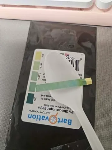 A photo showing a glucose testing strip on a plastic spoon that lies on top of the color strip.