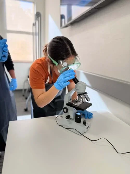 A photo showing a student in protective gear viewing a microplastics solution sample under a microscope.
