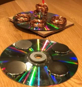 A photograph of the initial stages of the copper coil generator prototype. At bottom, a CD with magnets glued to the back; at top, another CD with copper coils glued to the back, and a red LED attached to the center of the generator.