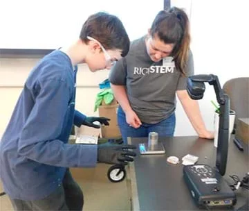 Teacher bent over a digital scale helping a student read the mass on the screen.
