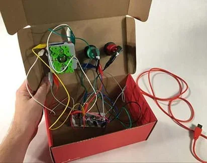A photograph shows the inside of the shoebox, displaying the undersides of the joystick and two arcade buttons amidst a mass of alligator clip wires and one USB cable.