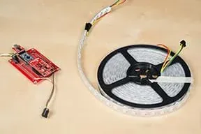 A photograph shows the completed circuit with the Thing board and Pro Mini attached to the breadboard; the barrel jack connector comes off the of breadboard and is not connected to the power source. The reel of LED lights is attached by wire and sitting off to the side.