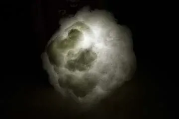A photograph taken in a dark room shows a paper lantern orb that is entirely obscured by glued-on white fluffy polyfil material and lit by a flashlight held in the center of the lantern/cloud.