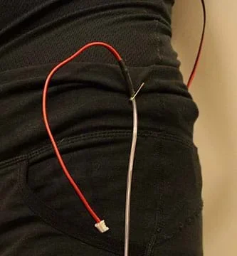 A photograph shows a safety pin holding a strand of red EL wire to the clothing on a woman’s back hip.