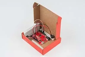 A photograph shows a lidded cardboard box containing the breadboard with the speaker, the RedBoard, and the breadboard with the potentiometer, all connected with wires.