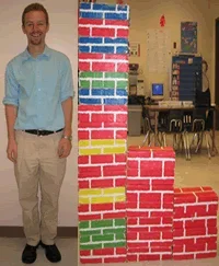 A photograph shows an adult standing next to a stack of shoebox-sized building blocks as tall as he is.