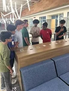 A photo showing seven students standing near a counter looking at the categories of 12 Ethics Twist Cards.