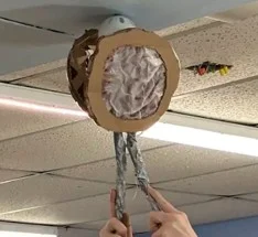 A photo showing a cardboard grasping device removing a wiffle ball that had been velcroed to the ceiling. 