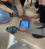 A photo showing two students sitting around an mBot2 robot and tablet they are programming.