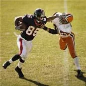 A photograph shows a football player with the ball giving a stiff-arm to another football player.