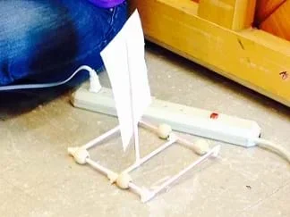 A photograph shows a sail car composed of a square frame made from taped drinking straws, four bead wheels and a square paper sail supported by a single mast positioned vertically in the middle of the sail base.