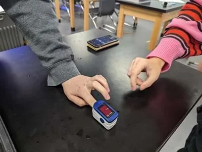 A photo of students measuring baseline heartrate using the simple oximeter alternative.