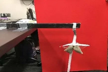 Prototype sled hockey stick taped 10 centimeters onto a table with weights connected 4 centimeters from the opposite end of the stick.