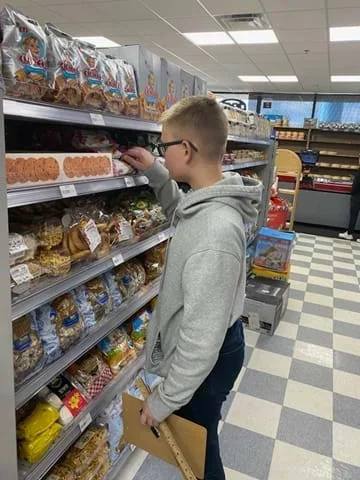 A photo showing a student holding a clipboard and a meter stick looking at a Turkish product on an eye-level shelf.