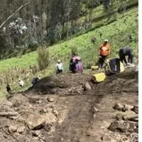 Photo of the minga from Yambiro working on a community project. They are moving bags of materials on the hill. The image shows the incline of the hill.